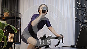 Woman is drinking water while cycling on indoor smart bicycle trainer