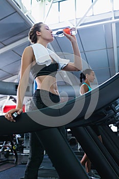 Woman drinking water while exercising on a treadmill in fitness center