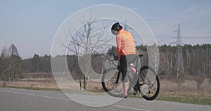 Woman is drinking water and preparing for ride on bike. Female cyclist in helmet drinks from bottle and starts training on bicycle