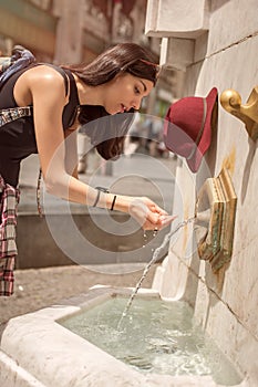 Woman drinking water at the public street fountain