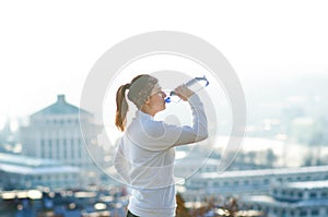 Woman drinking water during a running. Cold weather. Jogging woman in a city during a winter. Sunny day. Drinking mode.