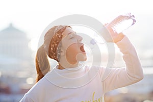 Woman drinking water during a running. Cold weather. Jogging woman in a city during a winter. Sunny day. Drinking mode.