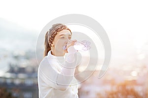 Woman drinking water during a running. Cold weather. Jogging woman in a city during a winter. Sunny day. Drinking mode.