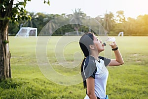 Woman drinking water after running exercise at the garden in sunset