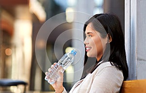 Woman drinking water sitting on wooden city bench