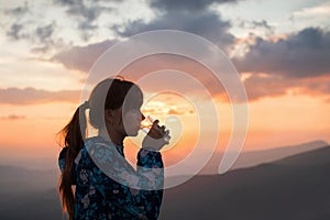 Woman drinking water on sunset background