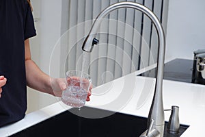 Woman drinking from water tap or faucet in kitchen. Pouring fresh water. Healthy lifestyle. Water quality check concept. The