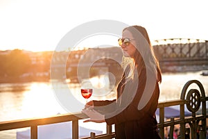 Woman drinking a wine in the city during a sunset. Glass of red wine. Concept of free time in the city and drinking alcohol.