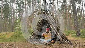 Woman drinks beverage from thermocup in hut among pine wood