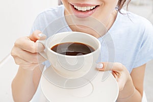 Woman drinks a black espresso coffee and smiles. The concept of problems with the color of teeth from bad habits