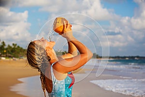A woman drinks coconut at the seashore at sunset
