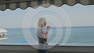 A woman drinks coffee on the balcony of a hotel with a beautiful view of the sea.