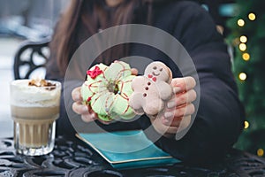 A woman drinks coffee with cream and eats Christmas macarons in a cafe outside.