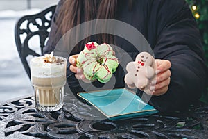 A woman drinks coffee with cream and eats Christmas macarons in a cafe outside.