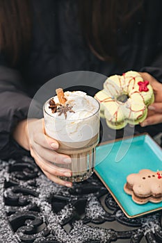 A woman drinks coffee with cream and eats Christmas macarons in a cafe outside.