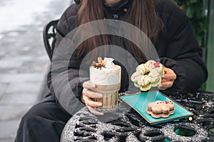 A woman drinks coffee with cream and eats Christmas macarons in a cafe outside.