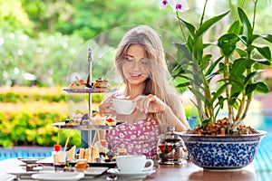 Woman drinks coffee or tea cup with desserts in outdoor restaurant