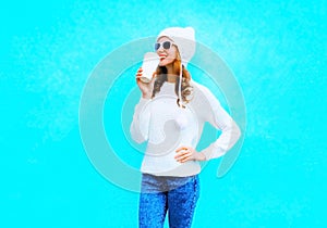 woman drinks coffee in white sweater, hat on a blue background