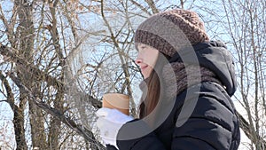 Woman Drinks Hot Tea or Coffee From a Cozy Cup on Snowy Winter Morning Outdoors. Beautiful Girl Enjoying Winter in a