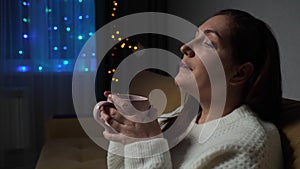 Woman drinks tea sitting on sofa in decorated living room