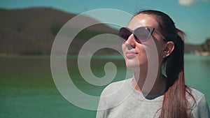 A woman drinks tea from a thermos in the sun, sitting on a wooden pier of the lake on a spring day, relaxing in nature.