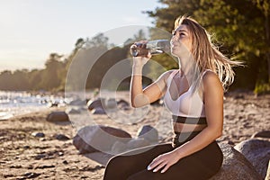 Female is drinking water from bottle on seaside.