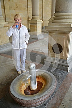 The woman drinks water from a mineral source in Karlovy Vary (focus on a source)