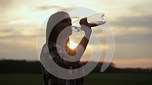 Woman drinks water from a plastic bottle on sunset. Woman quenches her thirst in nature