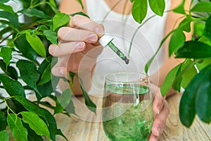 Woman dripping chlorophyll supplement into a glass of water. Selective focus.