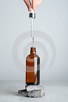 Woman dripping hydrophilic oil into bottle at white table, closeup