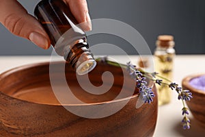 Woman dripping lavender essential oil from bottle into bowl, closeup