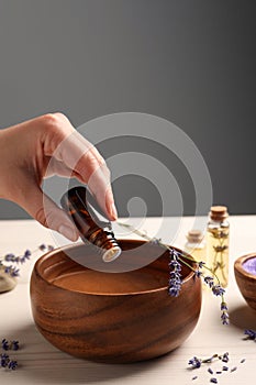 Woman dripping lavender essential oil from bottle into bowl at white wooden table, closeup. Space for text