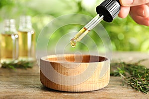 Woman dripping natural tea tree oil in bowl on table