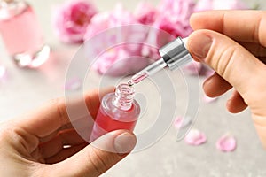 Woman dripping rose essential oil into bottle over table