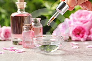 Woman dripping rose essential oil into bowl on table