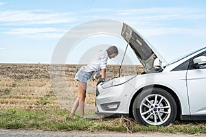 woman driver looking at the motor of her broken car outdoors