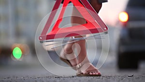 Woman driver putting an emergency stop sign behind  broken blurred car with blinking lights.