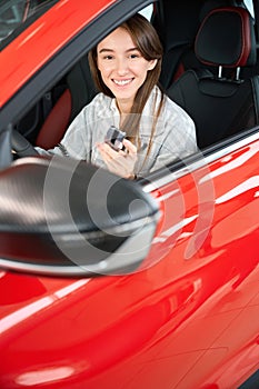 Woman driver showing car keys while sitting in her new automobile in dealership