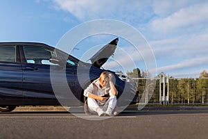 woman driver waiting for help from emergency tow truck near broken down car with open hood