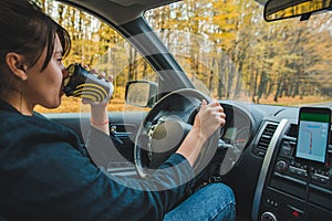 woman driving car by autumn speedway drinking coffee