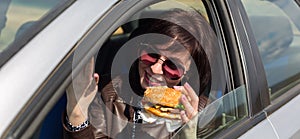 A woman driving a car with a burger waving her arms