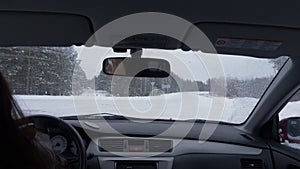 Woman driving car on crossroad and snowy road at winter day view from back seat