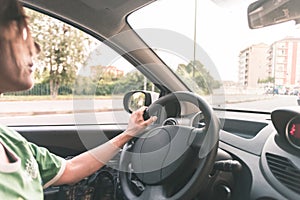 Woman driving car with hands on steering wheel. Interior close up, selective focus, side view, motion blurred on street.