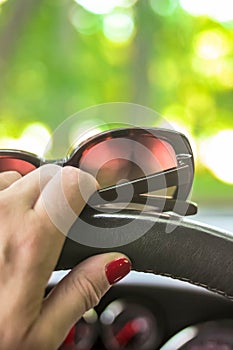 Woman driving a car with one hand holding the steering wheel and sunglasses
