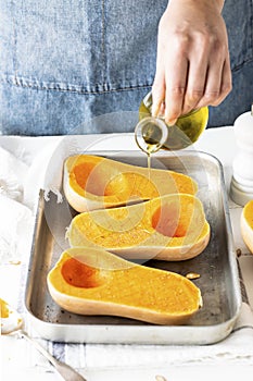 Woman drizzling olive oil over butternut squash before baking