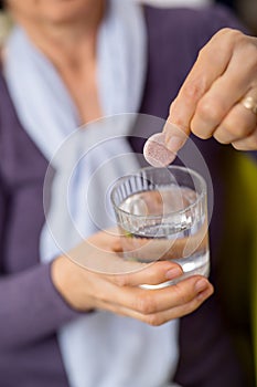 Woman dropping an effervescent antacid in a glass of water
