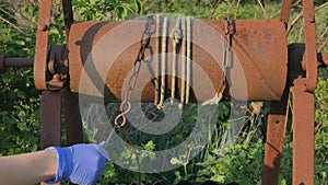 Woman drops chain with bucket into rustic well to draw water. Vintage water well chain close up. Old rusty chain of the