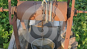 Woman drops chain with bucket into rustic well to draw water. Vintage water well chain close up. Old rusty chain of the