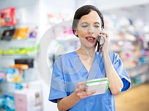 Woman druggist making notes and talking on phone