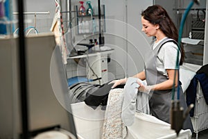 Woman dry-cleaning operator carefully inspecting clothes by hand